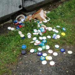 Viele Einmachgläser-Deckel liegen vor einem Glascontainer auf dem Boden