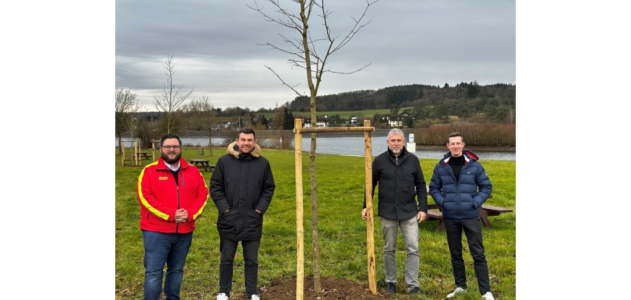 An der Badestelle Aartalsee neben einem frisch gepflanzten Baum stehend, von rechts nach links: Lukas Schöne, Leiter Fielmann-Niederlassung Herborn, Bürgermeister Marco Herrmann, Jan Kunz vom Bauamt der Gemeinde Bischoffen und Michael Dimmer, OG DLRG Aartalsee